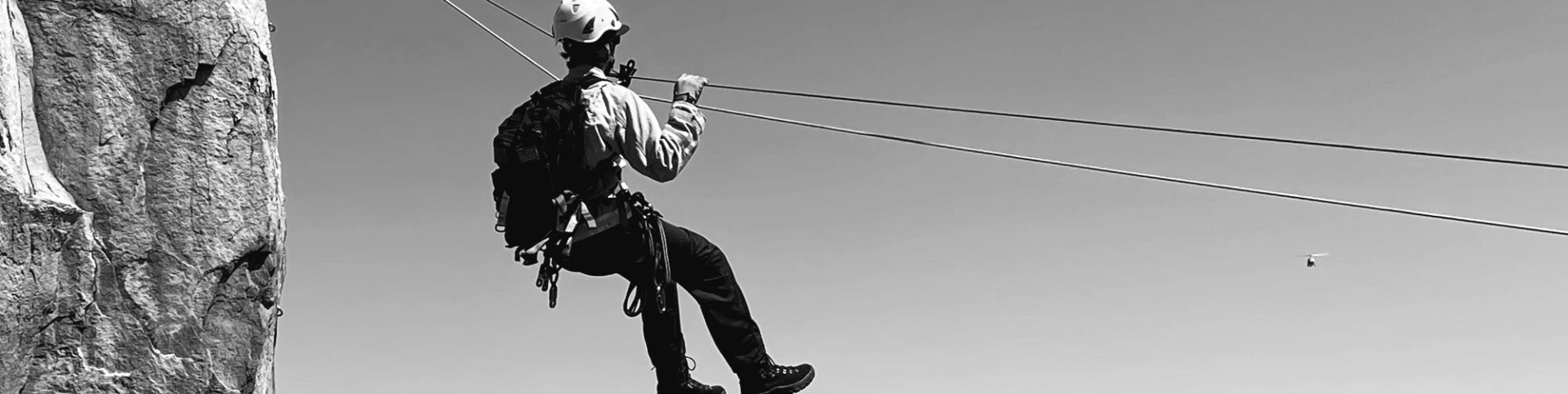 man ziplines near cliff with helicopter in sky